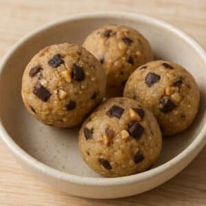 Close-up of keto cookie dough bites with chocolate chunks and walnuts in a ceramic bowl on a wooden surface.