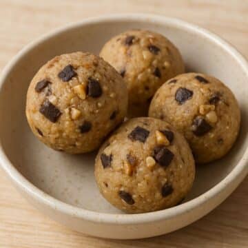 Close-up of keto cookie dough bites with chocolate chunks and walnuts in a ceramic bowl on a wooden surface.