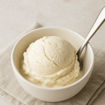 A scoop of homemade keto vanilla ice cream in a white bowl with a spoon, set on a neutral linen napkin.