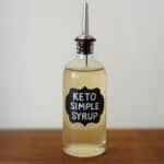 Glass bottle labeled keto simple syrup with metal pour spout on wooden counter