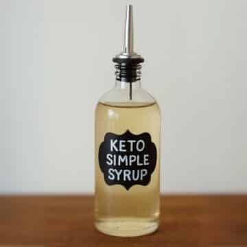 Glass bottle labeled keto simple syrup with metal pour spout on wooden counter
